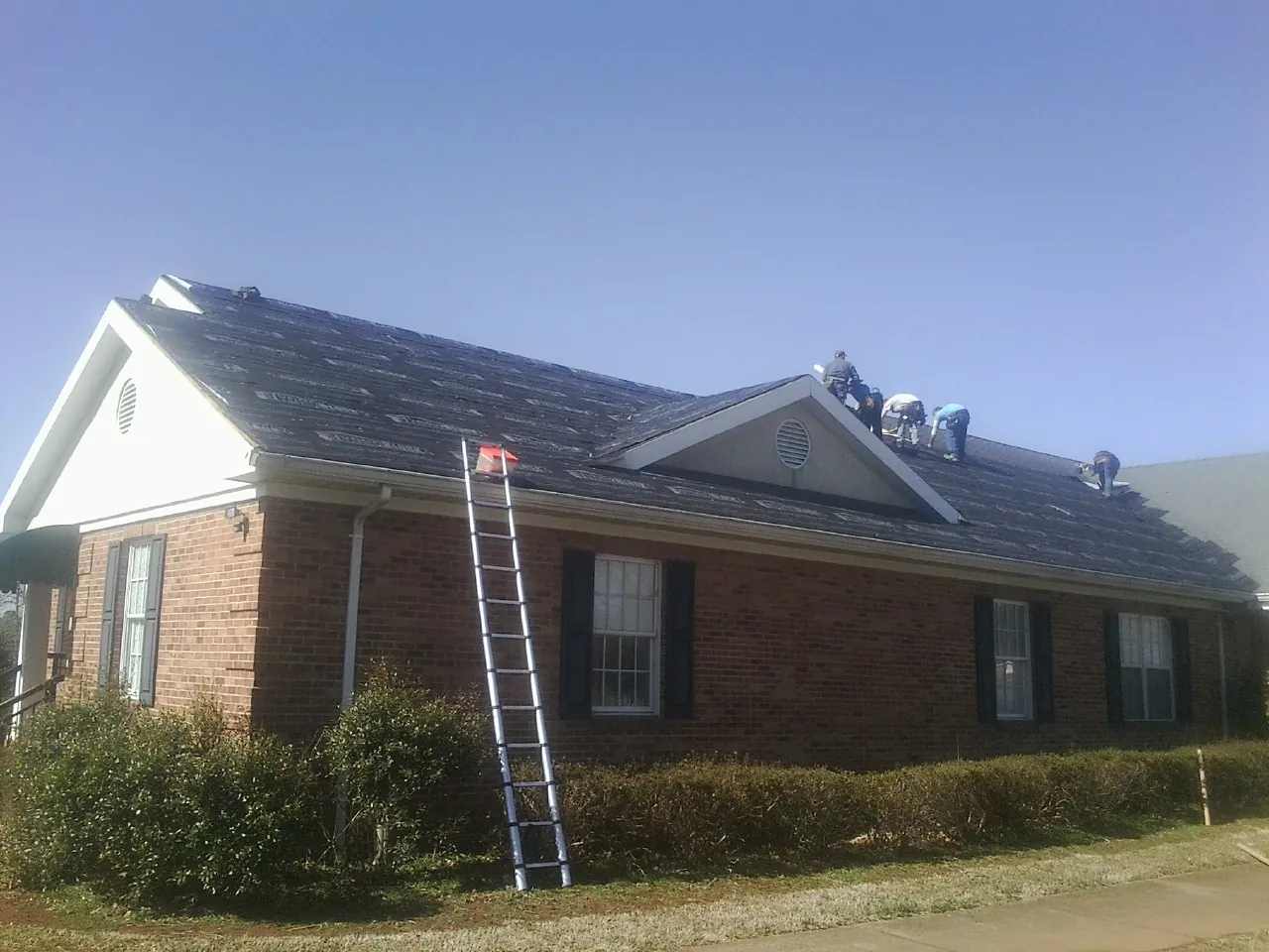 Crew tearing shingles off a brick ranch roof with a ladder set — Metal Roof Repair work by our crew in Tyner