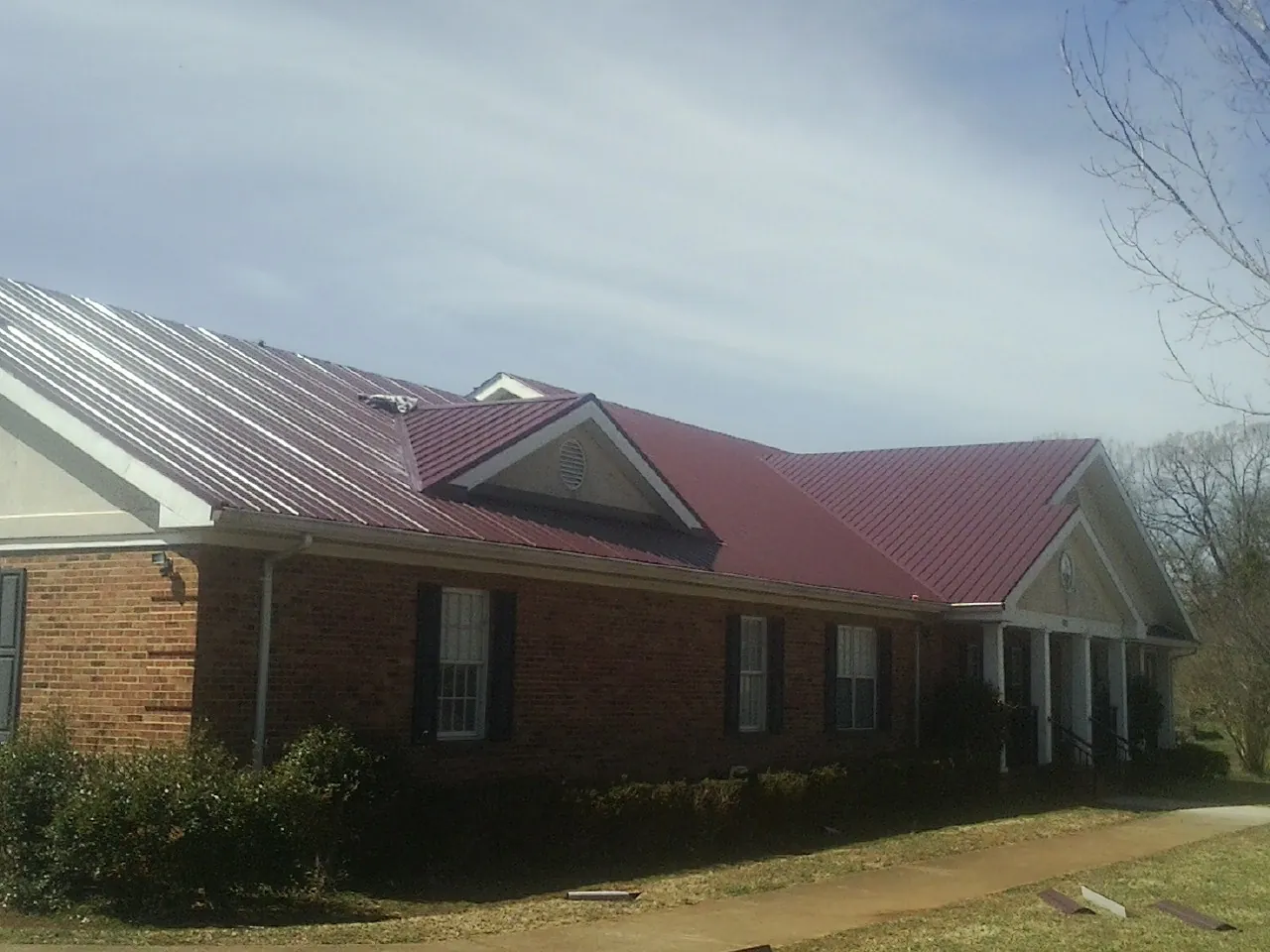 Red metal roof with gabled entries on a long brick building, from a Hail Damage Roof Repair job in Tyner