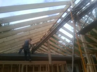Rafters going up over a new addition with a worker on the wall in Tyner