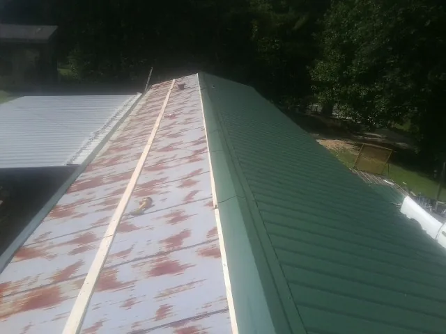 Old rusted panels beside newly installed green metal roofing — Wind Damage Roof Repair by Roofing Brothers in Tyner