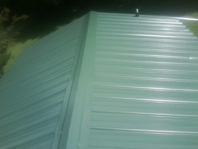 New green metal panels meeting at the ridge of a roof — Flat Roof Repair work by our crew in Tyner