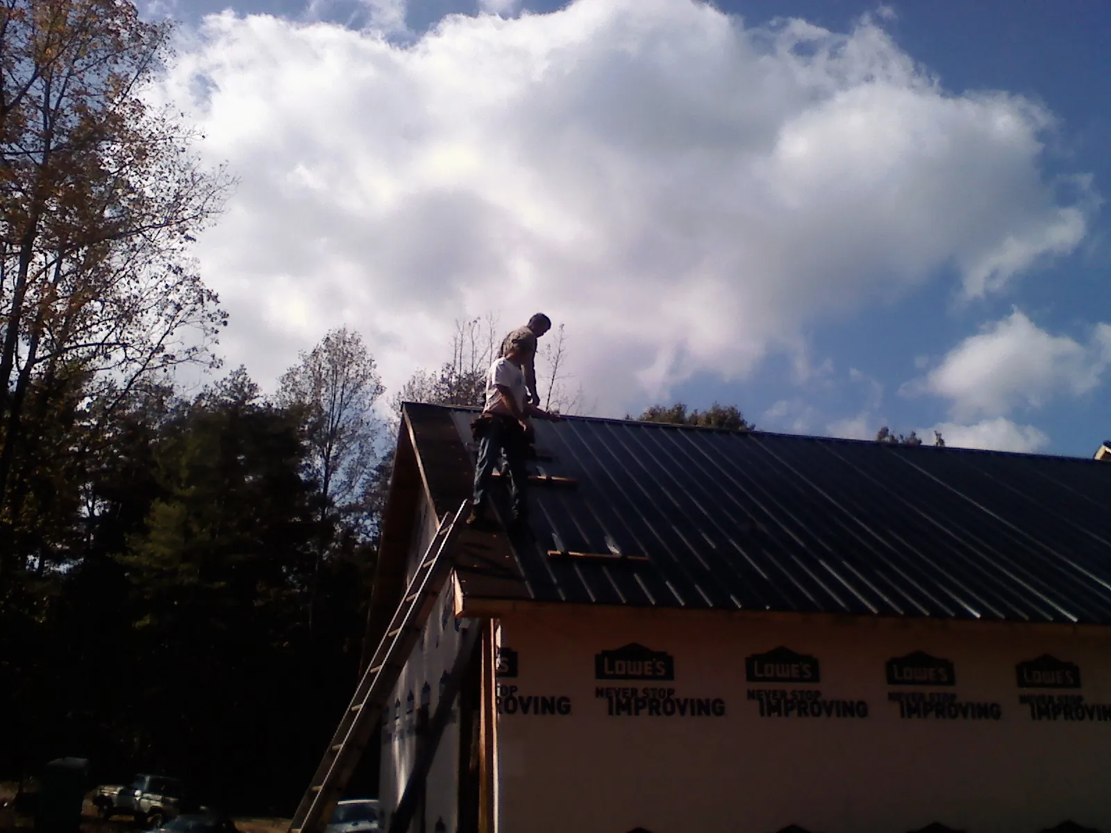Roofer fastening dark metal panels high against a cloudy sky, from a Roof Inspection job in Tyner
